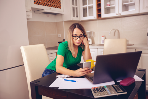 Single mom working - Stressed businesswoman working at the kitchen table with laptop and calculator